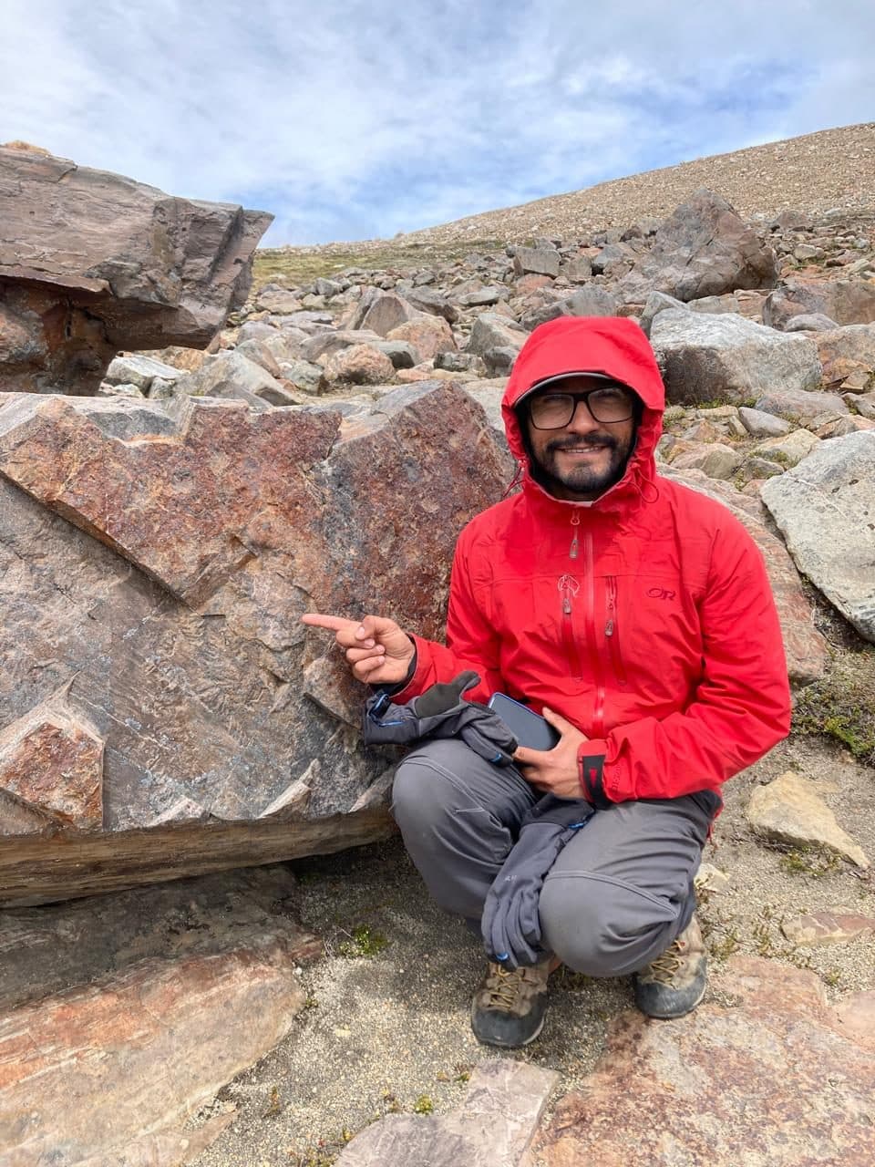 Retrato de Pablo Azúa, geólogo, con chaqueta roja junto a un afloramiento rocoso.