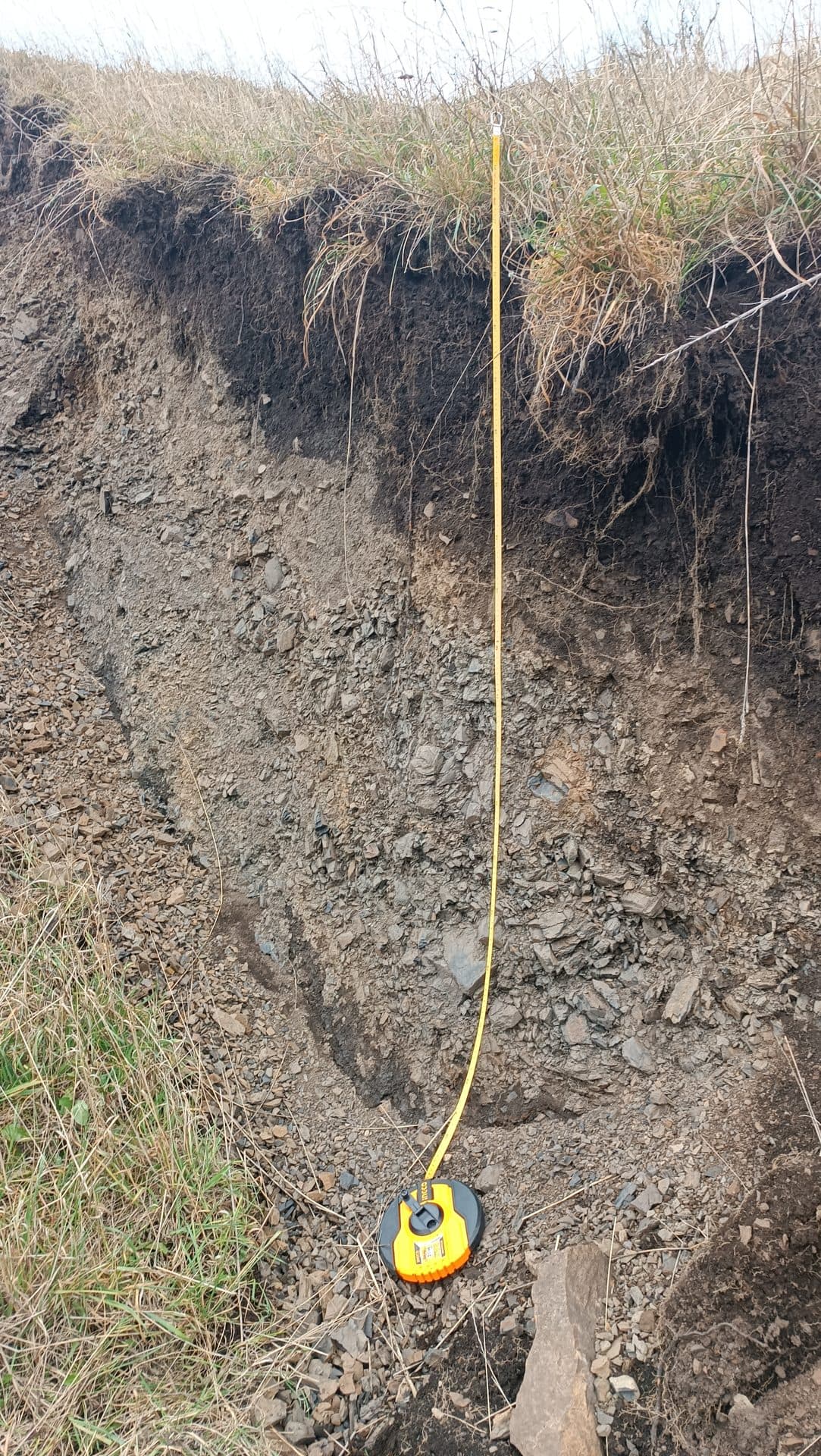 Escarpe de un talud medido con cinta métrica durante un levantamiento geológico.